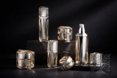 Clear faceted acrylic skincare bottles and cosmetic jars with neutral interiors, arranged on dark blocks with open bottle.