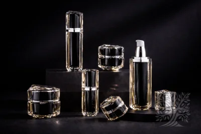 Clear faceted acrylic skincare bottles and cosmetic jars with black interiors, displayed on dark platform with open bottle detail.