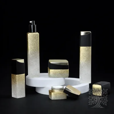 Frosted gold-to-clear gradient bottles and jars with black caps, displayed on white risers with lids set aside.