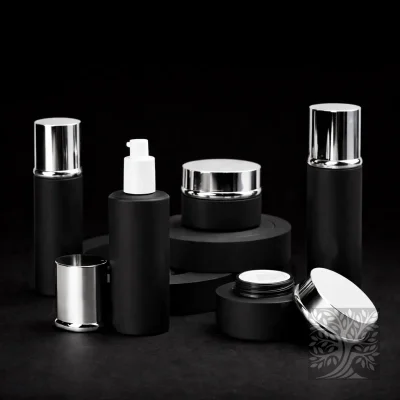 Matte black skincare bottles and cosmetic jars with silver caps, arranged on tiered black platforms with spare lids.