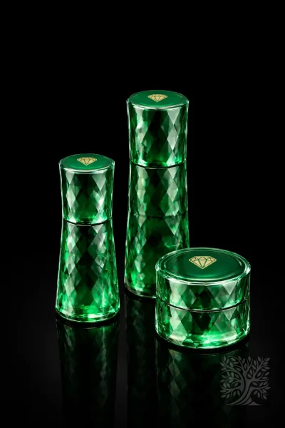 Emerald green faceted acrylic skincare bottles and cosmetic jar with glossy finish, displayed on reflective black base.