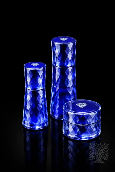 Solid cobalt blue faceted acrylic skincare bottles and cosmetic jar set with reflective finish on black background.