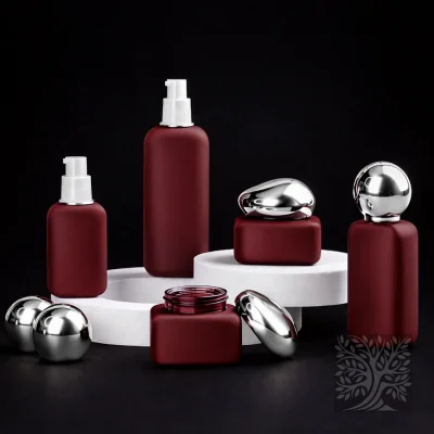 Matte burgundy glass bottles and cosmetic jars with silver caps, displayed in a clean Macigno packaging arrangement on a platform.