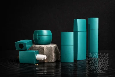 Teal glass serum bottles and cosmetic jars with soft matte finish, arranged in a balanced composition on reflective water.