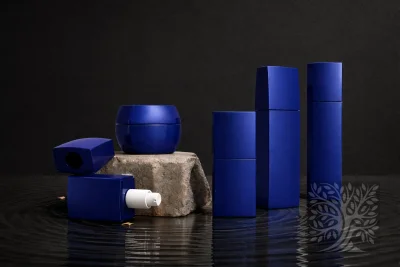 Cobalt blue skincare bottles and cosmetic jars with rounded jar and square bottles, arranged on a stone platform and reflective surface.
