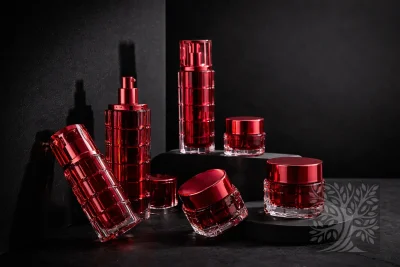 Glossy red acrylic skincare bottles and cosmetic jars with matching red caps, staged on black blocks with angled jar display.