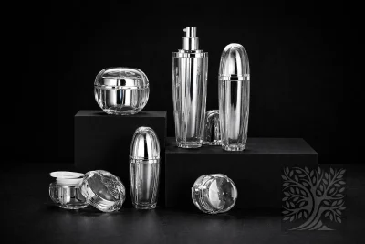Clear faceted acrylic skincare bottles and cosmetic jars with chrome accents, arranged on black blocks with open jar detail.