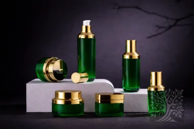 Emerald green acrylic skincare bottles and cosmetic jars with gold caps, arranged on white platforms with mixed bottle sizes.